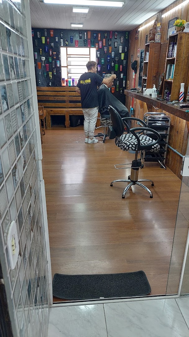 Interior da Barbearia Hollywood com o barbeiro atendendo um cliente no fundo do salão